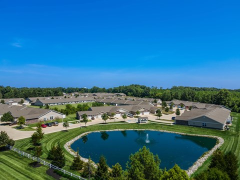 A large pond in the middle of a grassy area surrounded by houses.