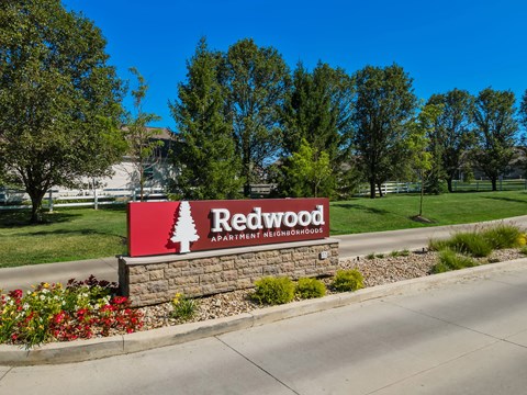 A sign for Redwood Apartment Neighborhoods is displayed in front of a grassy area.