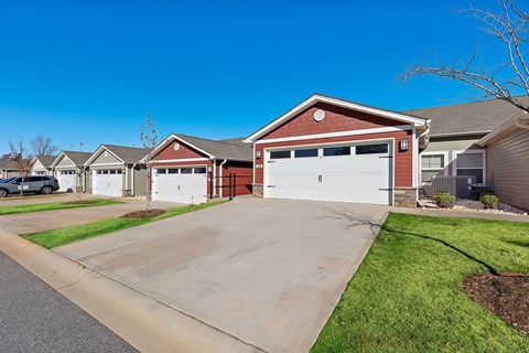 A red house with a white garage door is in front of other houses.
