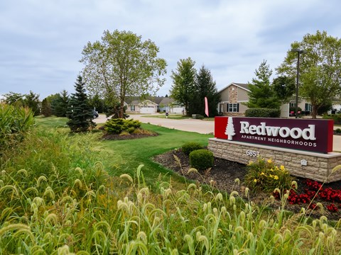 A sign for Ratwood Apartment Neighborhoods is in the foreground of a well-kept lawn.