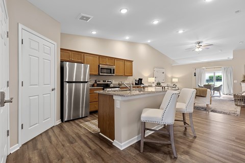A kitchen with a refrigerator, microwave, and a counter with two chairs.