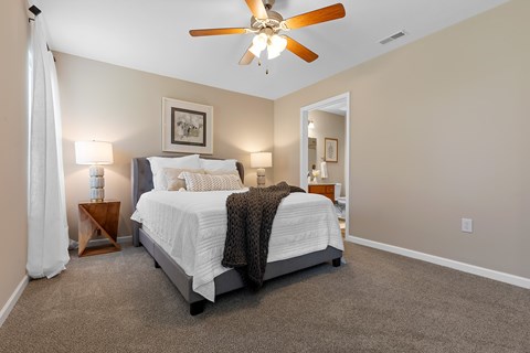A bedroom with a bed, a ceiling fan, and a nightstand with a lamp.