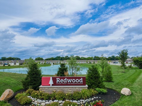 A sign for Redwood Apartment Neighborhood sits in front of a grassy area with a lake in the background.