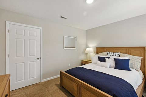 A bedroom with a bed, nightstand, lamp, and door.
