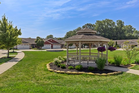 A gazebo is surrounded by a flower bed in a grassy area.
