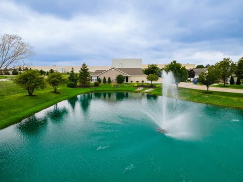 A fountain in the middle of a pond in front of a building.