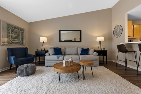 A living room with a grey couch, a blue chair, a wooden coffee table, and a mirror on the wall.