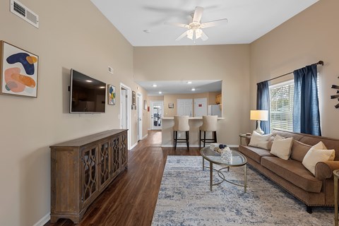 A living room with a brown couch, a glass coffee table, and a ceiling fan.