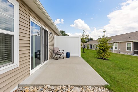 A patio with a table and chairs is surrounded by a grassy area and other houses.