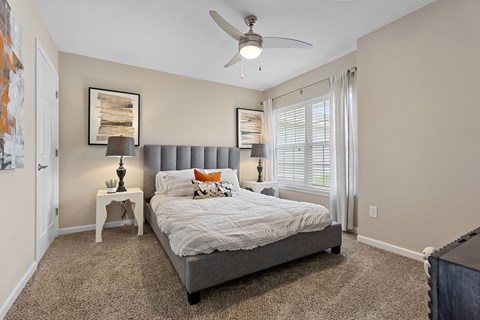 A bedroom with a bed, a ceiling fan, and a small table with a lamp on it.