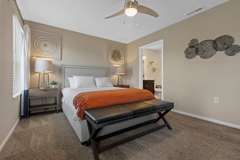 A bedroom with a bed, a bench, and a ceiling fan.