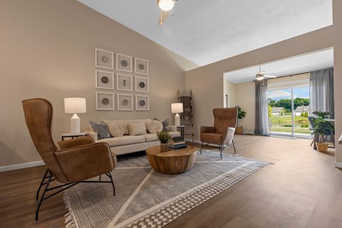 A living room with a grey sofa, a wooden coffee table, and a large window with a view of the outdoors.