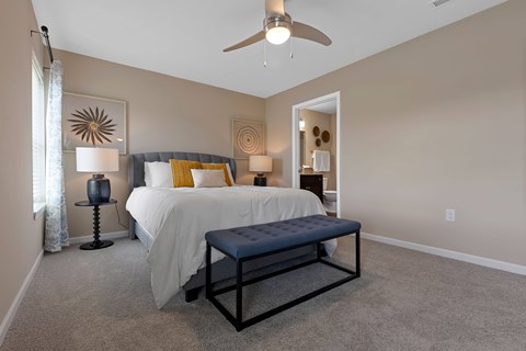 A bedroom with a bed, a bench, and a ceiling fan.