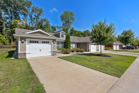 A residential house with a white garage door is surrounded by a well-maintained lawn and a clear blue sky.
