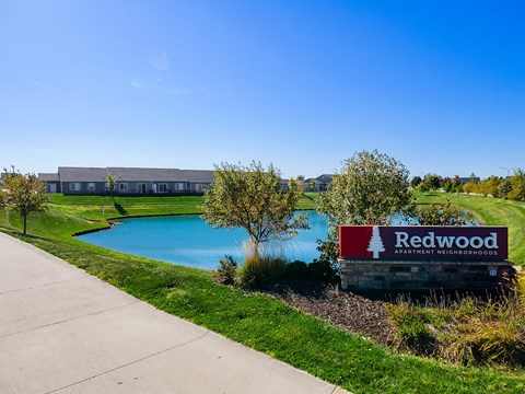A sign for Redwood Apartment Residences is in front of a building and a pool.