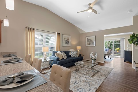 A dining room with a table set for two and a couch in the background.