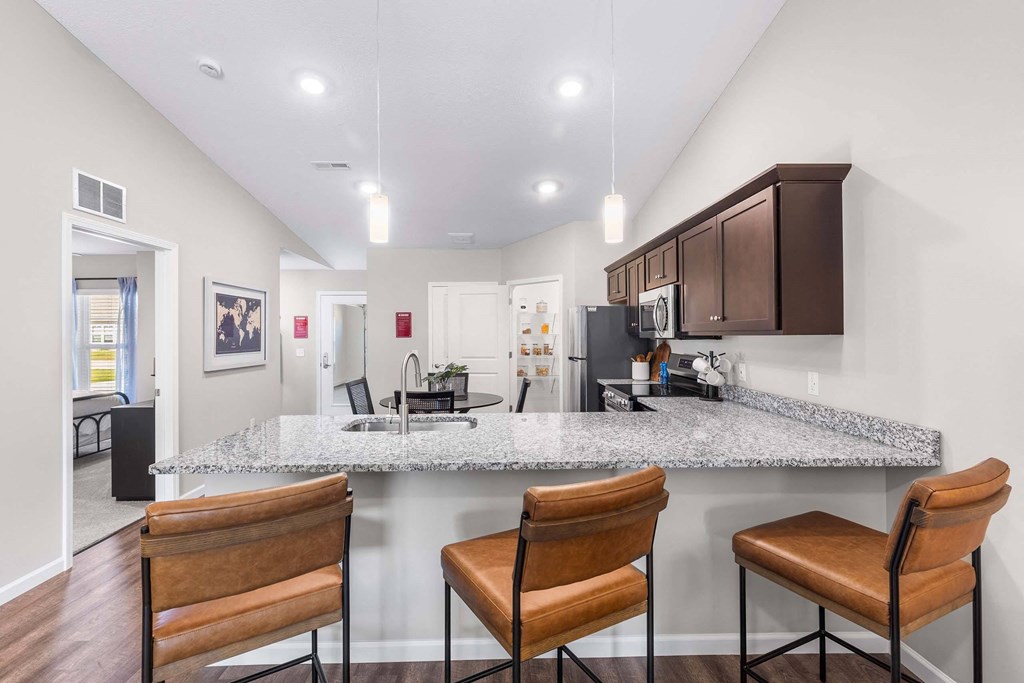 A kitchen with a granite countertop and brown chairs.