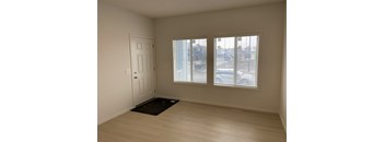 A room with a door, a window with blinds, and a mat on the floor.