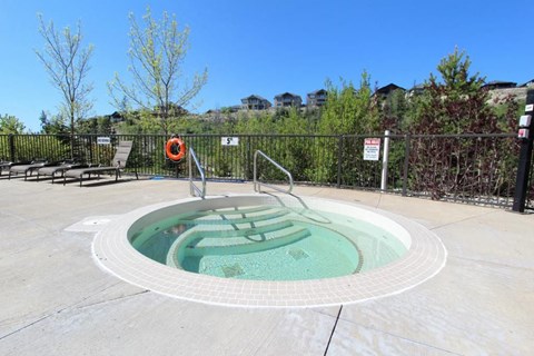 A hot tub sits in the middle of a patio surrounded by a black fence.