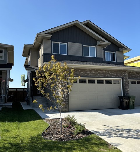 A house with a grey garage door and a tree in front.
