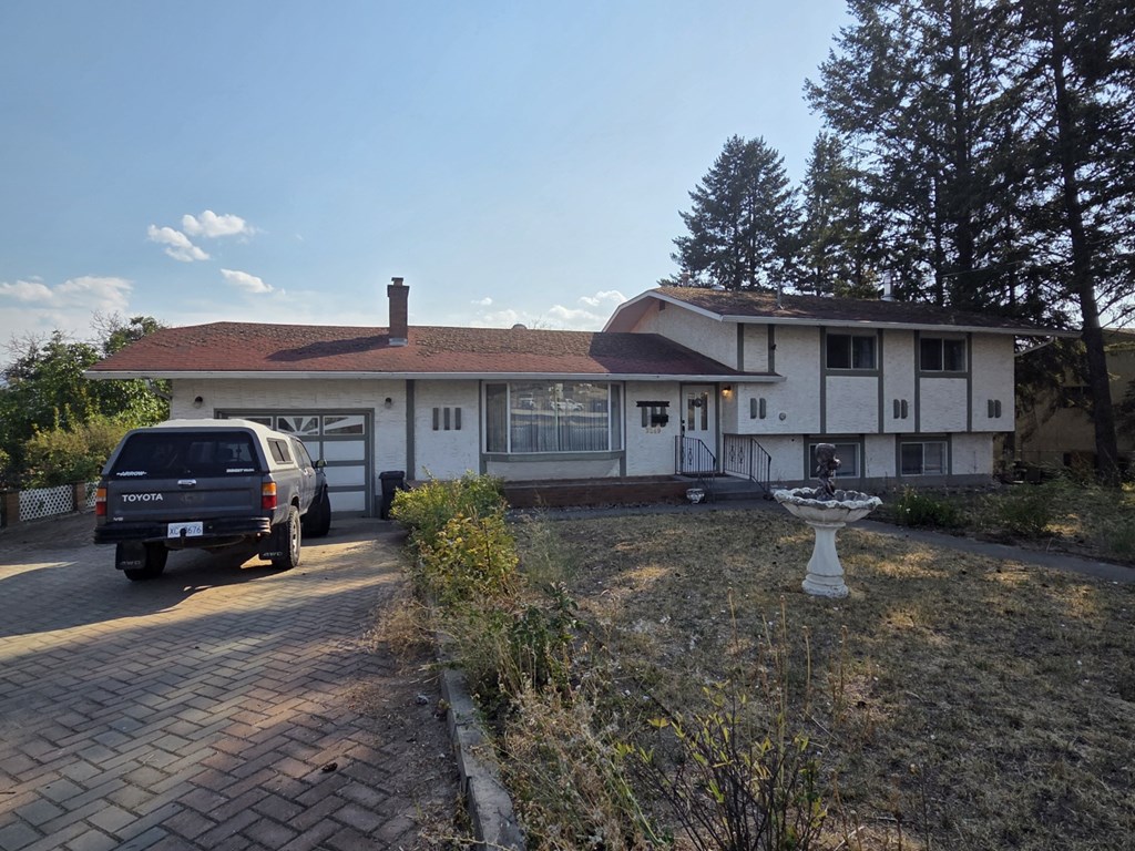 A house with a white exterior and a brown roof is shown with a car parked in front.