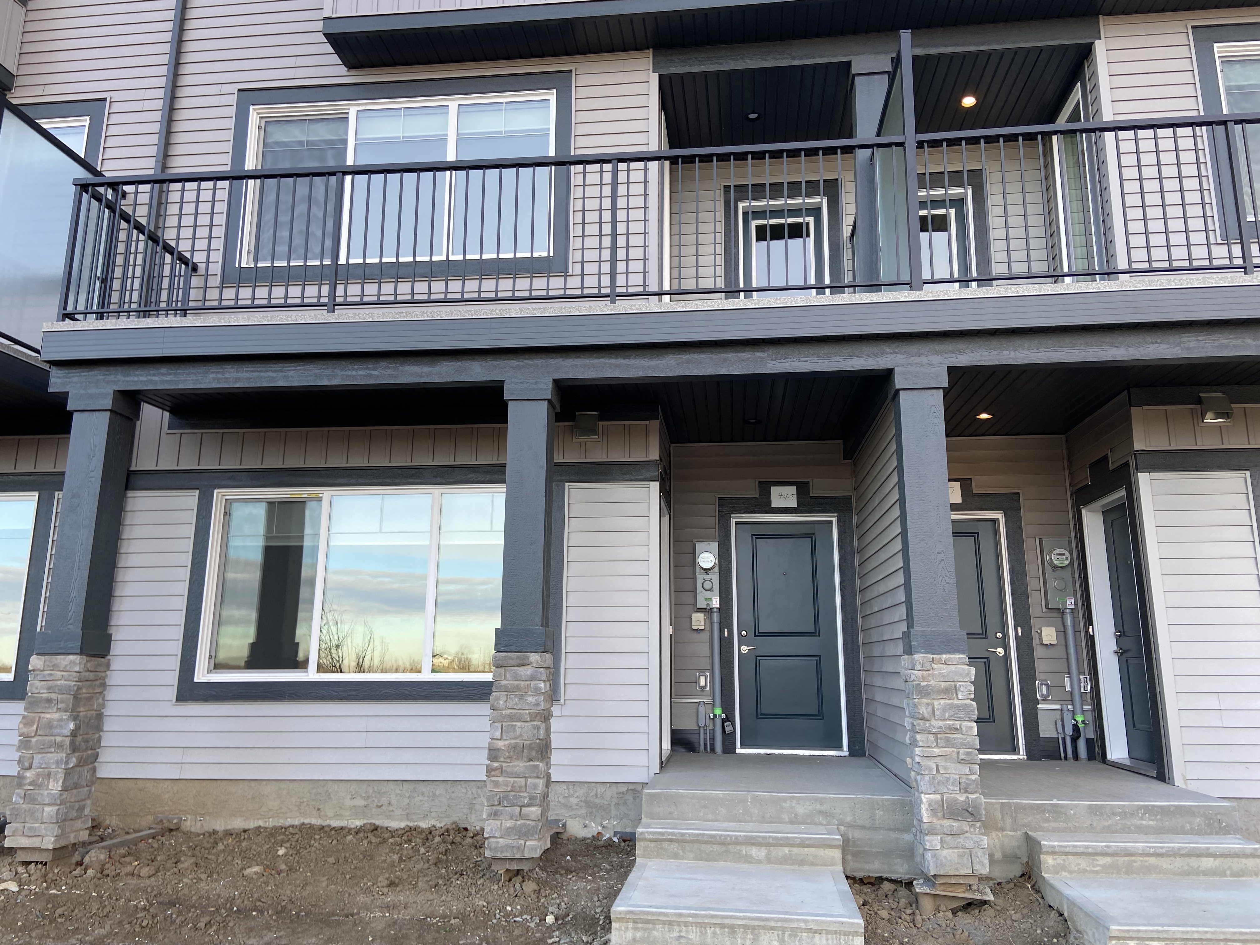 A grey house with a balcony and a black door.