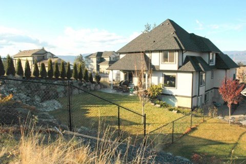 A house with a white exterior and a black roof is surrounded by a fence and trees.