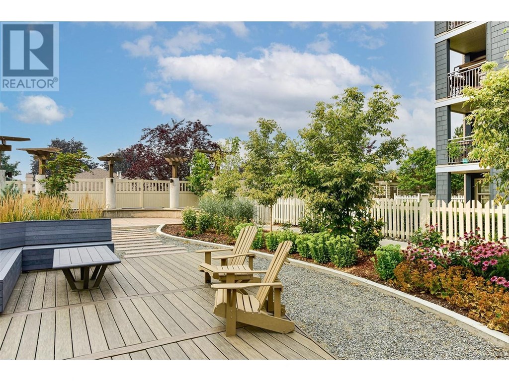 A wooden deck with a bench and a chair is surrounded by a gravel path and a white picket fence.