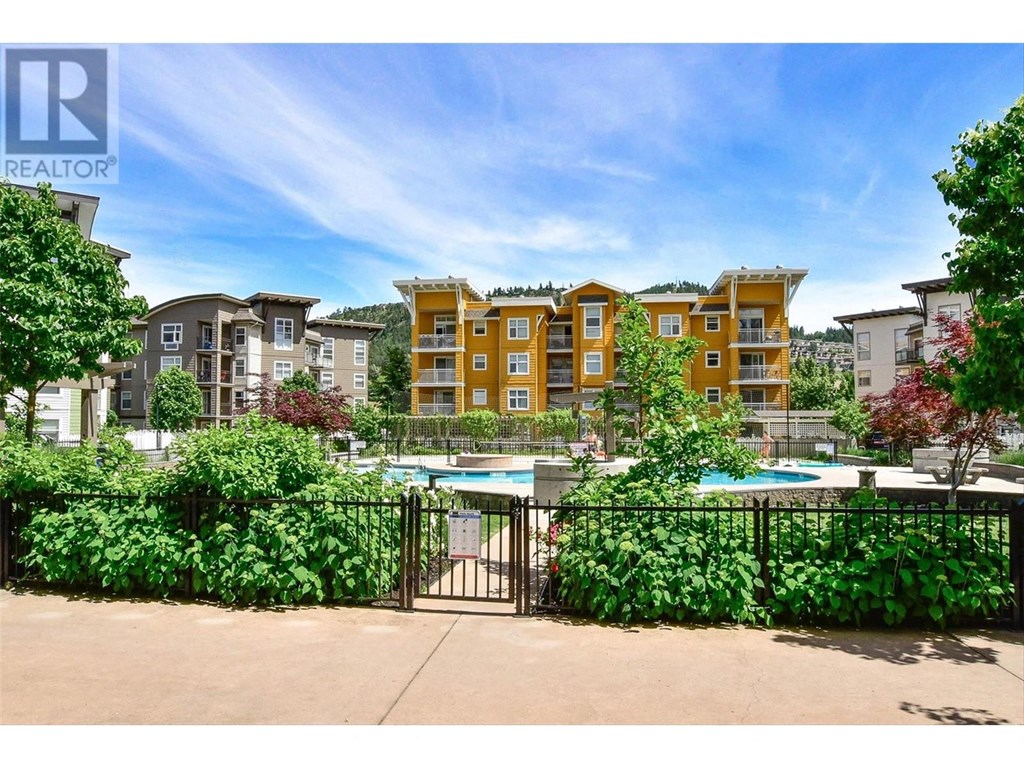 A pool surrounded by a black fence and green plants with apartment buildings in the background.