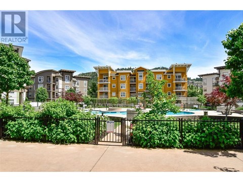 A pool surrounded by a black fence and green plants with apartment buildings in the background.