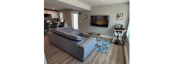 A grey couch sits in a living room with a blue rug and a white table.