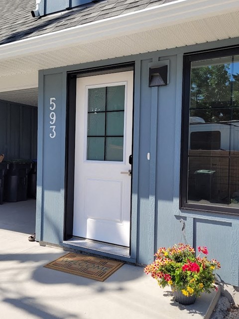 A white door with a glass window is on a grey house.
