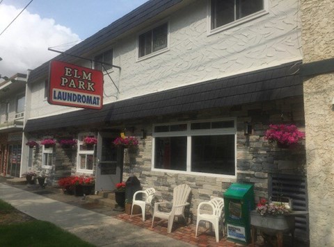 A laundromat named Elm Park is shown with white chairs and pink flowers outside.