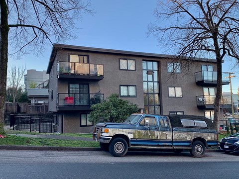 A blue pickup truck is parked on the side of a street in front of a building.