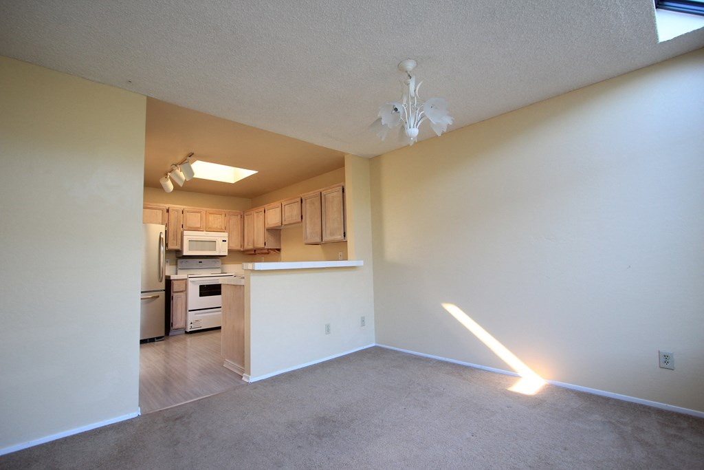 an empty living room with a kitchen in the background