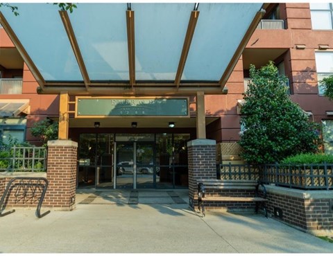 The entrance to a building with a glass canopy and a brick pillar.