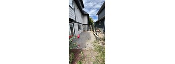 A backyard with a concrete pathway, a small garden, and a house.