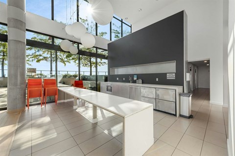A modern kitchen with a long white island and red chairs.