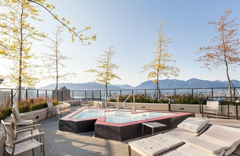 A hot tub is surrounded by chairs on a patio with trees and mountains in the background.