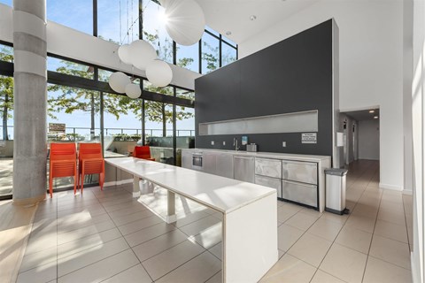 A modern kitchen with a long white island and red chairs.
