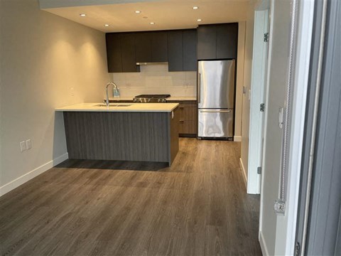 A modern kitchen with a stainless steel refrigerator and wooden flooring.