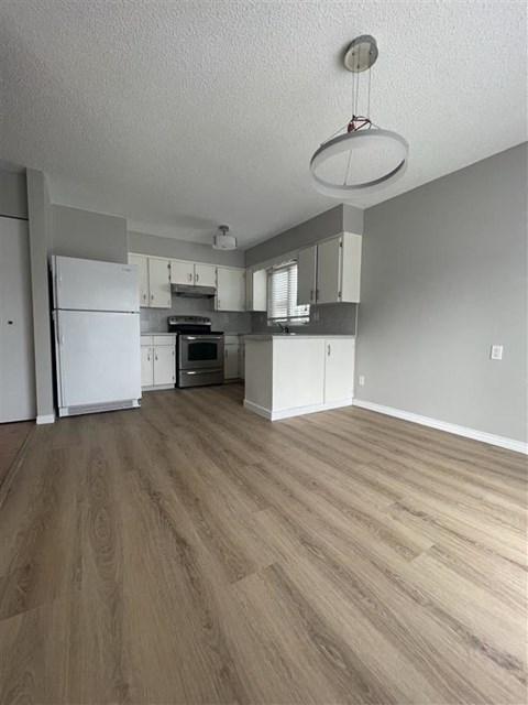an empty kitchen with white appliances and a wood floor