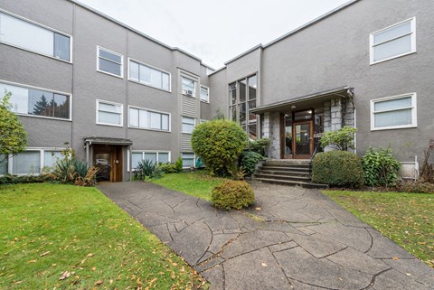 the front of a grey apartment building with a walkway