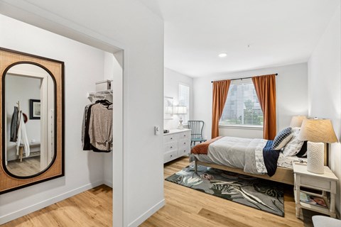 Bright bedroom with bed, dresser, open closet and window at Willowstone Apartments in Marysville, WA.