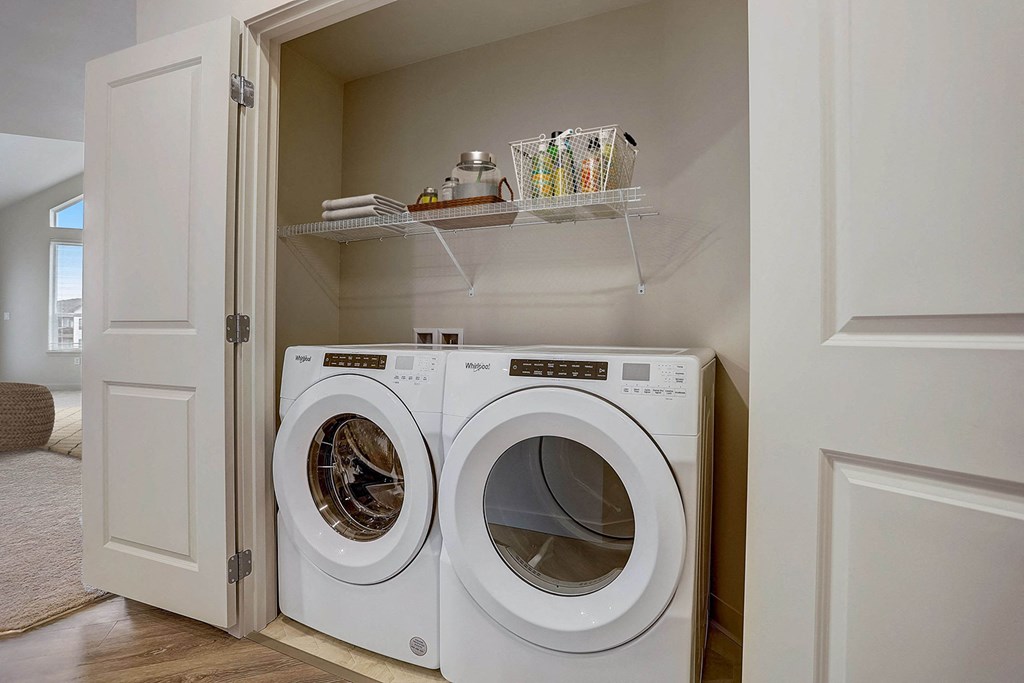 A white washing machine is in a cabinet under a shelf.