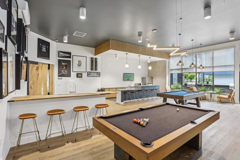 A pool table is in the middle of a room with a bar and stools.