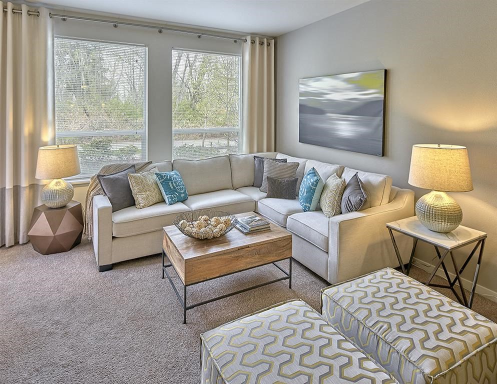 A living room with a large window, a sofa, a coffee table, and a side table with a lamp.