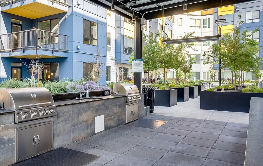 an outdoor patio with barbecue grills and plants in front of an apartment building