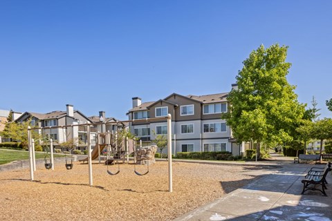 A playground with swings and a slide in front of apartment buildings.