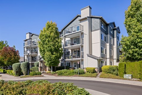 A large, modern apartment building with a well-maintained lawn and trees in front.